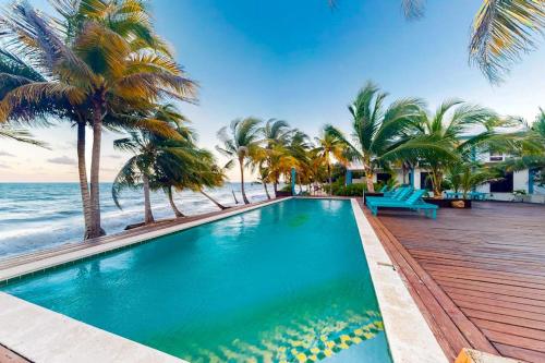 a swimming pool next to the ocean with palm trees at Charming beachfront condo with a kitchenette shared pool WiFi & beach access in Placencia