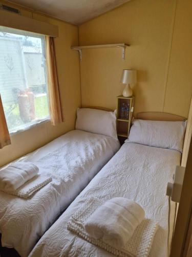 two beds in a small room with a window at Cabin Sleeps 6 with access outdoor Pool in Sandown