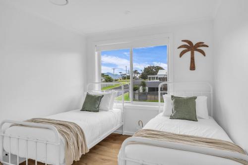 two beds in a white room with a window at Callow Place 10 in Bermagui