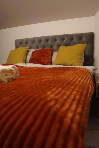 a large bed with an orange comforter and yellow pillows at Om relax apartman in Prijedor