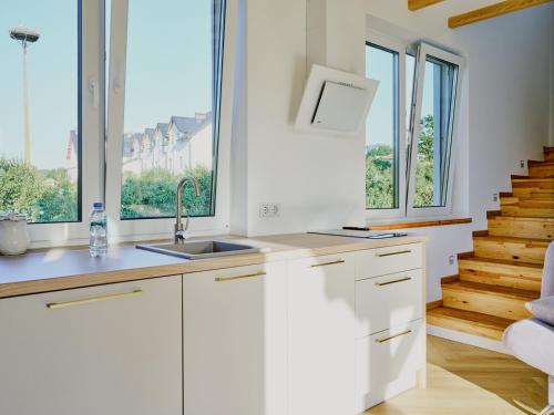 a kitchen with white cabinets and windows and a staircase at Domki Różane Nad Stawem in Stopnica