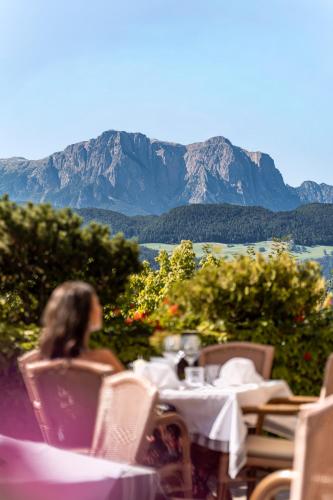 a woman sitting at a table with a view of mountains at Granpanorama Hotel StephansHof in Villandro