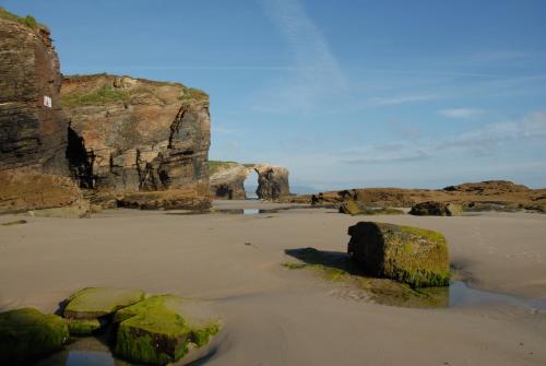 a beach with rocks in the sand and a cave at Hotel Playa de las Catedrales in Reinante