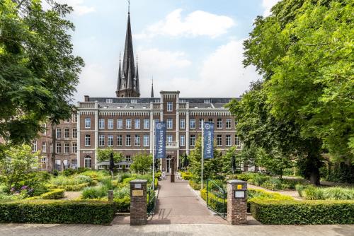 ein Gebäude mit einem Turm inmitten eines Gartens in der Unterkunft MERICI Hotel Sittard in Sittard