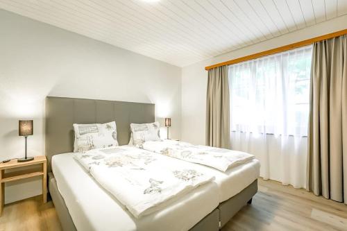 a white bedroom with a large bed and a window at Lauberhorn Apartment - Aare Jungfrau AG in Grindelwald
