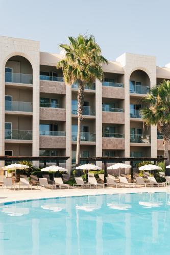 a hotel with a swimming pool with chairs and umbrellas at Falésia Hotel - Adults Only in Albufeira