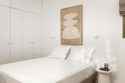 a white bedroom with a white bed and a painting at Halo Tinos - ARTEMIS in Tinos