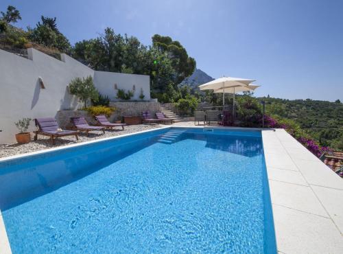 a pool with chairs and an umbrella next to a house at Elegant villa in Podgora with private pool and sea view in Podgora