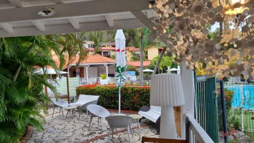 a patio with white chairs and an umbrella at Studio charmant à Sainte-Anne de 25 m² avec terrasse et jardin. in Sainte-Anne