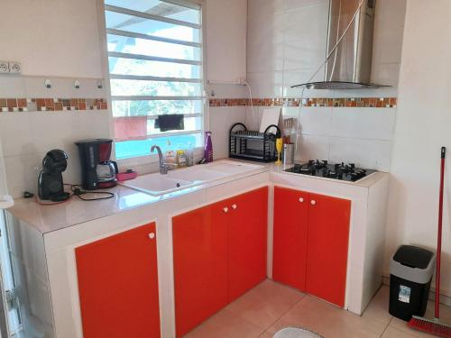 a kitchen with red cabinets and a sink and a window at Maison charmante à Petit-Bourg avec piscine partagée in Petit-Bourg