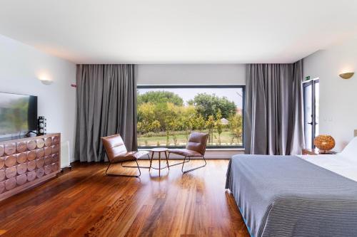 a bedroom with a bed and two chairs and a large window at Penedo Escape Sea Suites in Colares