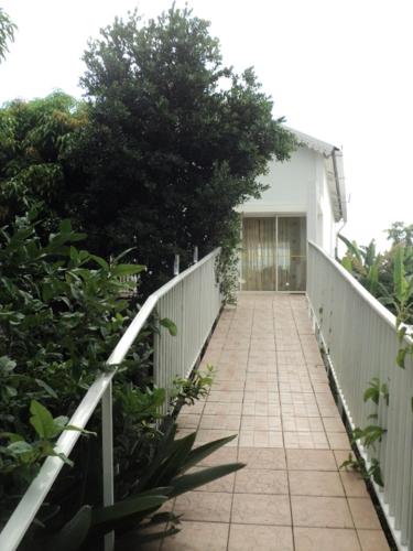 a walkway leading to a white house with a fence at Appartement spacieux à Bois des Nèfles, 70 m², piscine partagée in Le Bois de Nèfles