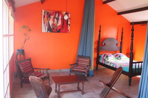 a bedroom with orange walls and a bed and chairs at Bungalow charmant avec vue sur la mer à Sainte Rose in Sainte-Rose