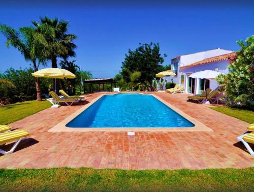 a pool with chairs and umbrellas next to a house at Elegant villa with sea view in Loulé + private pool in Loulé