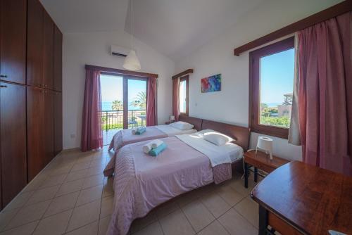 a bedroom with two beds and a table and windows at Ocean Breeze Club-Villa Mare in Kato Yialia
