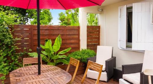 a wooden table with a red umbrella on a patio at Appartement Privilégié Le Moule 70 m² + Piscine in Le Moule
