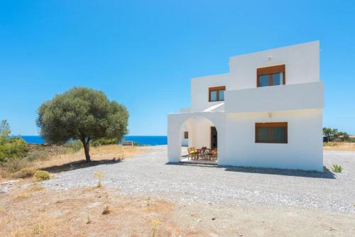 a white house with a tree and the ocean at Cosy House in Kiotari with Garden and Terrace in Kiotari