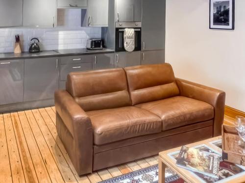 a brown leather couch in a living room with a kitchen at Stewards Bothy - Uk48303 in Berwick-Upon-Tweed