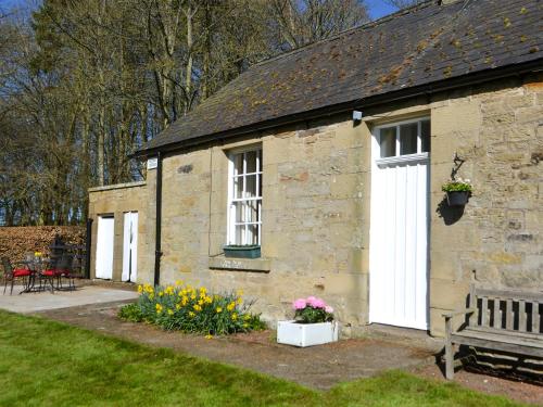 a stone building with a bench and flowers in a yard at Keepers Cottage Burradon in Sharperton
