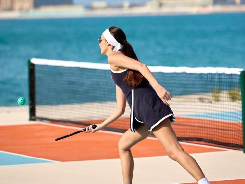 a woman holding a tennis racket on a tennis court at SO Ras Al Khaimah Hotel & Resort-Ultra All Inclusive in Ras al Khaimah