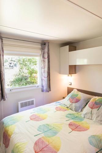 a bedroom with a bed with a colorful comforter and a window at Camping Sud Ardèche 3 étoiles familial piscine chauffée Gorges de l Ardèche Saint Remèze in Saint-Remèze