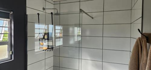 a glass shower in a bathroom with white tiles at Volgenoeg Self Catering Cottage in Oudtshoorn