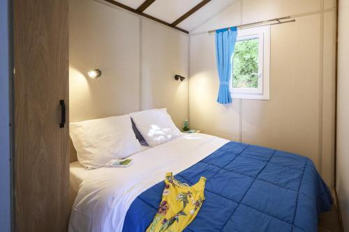 a bedroom with a bed with a blue comforter and a window at Camping les Chalands Fleuris in Saint-André-des-Eaux