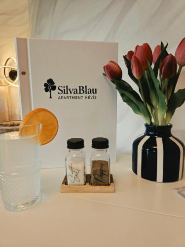 a table with a vase of red tulips and a glass of water at SilvaBlau Apartment Hévíz in Hévíz