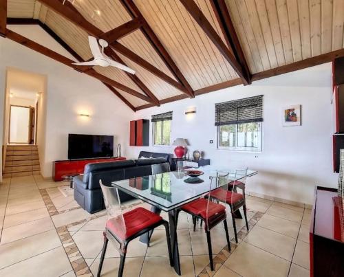 a living room with a glass table and red chairs at Villa Perle de lOcéan Piscine - Clim in Les Avirons