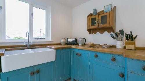 a kitchen with blue cabinets and a sink and a window at Brendon in Nefyn