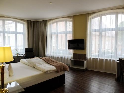 a bedroom with a bed and a tv and windows at Fründts Hotel in Wismar