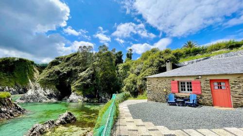 a house with two blue chairs next to a river at The Cliffs - Cala Porto do Val in O Vicedo