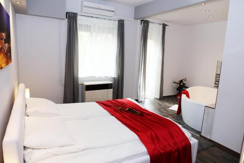 Un dormitorio con una cama blanca con una manta roja. en Velnök Luxus Apartman, en Makó