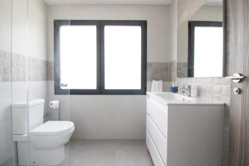 a bathroom with a toilet and a sink and two windows at La Morada de Sasa Casa tierra in Torrent