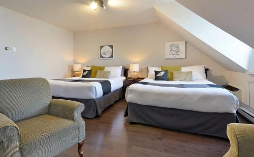 a hotel room with two beds and a chair at Hotel Cap-aux-Pierres in L'Isle-aux-Coudres