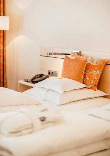 a bed with white sheets and orange pillows at Hotel Bayerischer Hof in Lindau