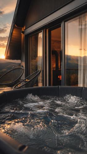 a hot tub on the balcony of a house with the sunset at Klek 77 Luxury Chalets near Jahorina in Paočići