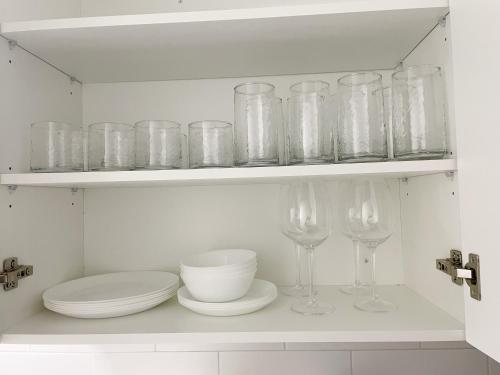 a white kitchen with glasses and plates on a shelf at Cozy 1 Br Apt with TV, Workstation, Kitchenette & Parking in Mississauga