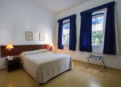 a bedroom with a bed and two windows at Vitória Palace Hotel in Lavras