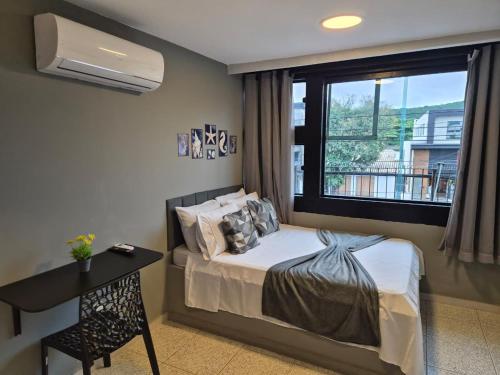 a bedroom with a bed and a desk and a window at CaisSuites in Cabo Frio