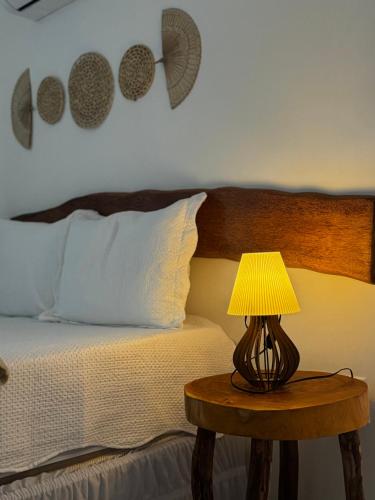 a bed with a table with a lamp on it at Pousada Vila Mar Japaratinga in Japaratinga