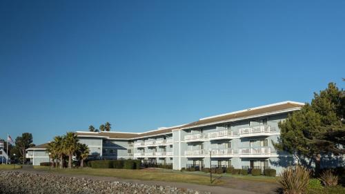 a large white building with balconies and palm trees at The Marina Inn on San Francisco Bay in San Leandro