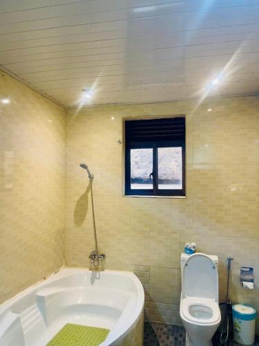 a bathroom with a tub and a toilet and a window at Gmasters Boutique Hotel in Kigali