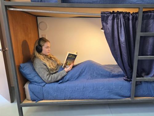 a woman sitting in a bed reading a book at Casa Centro Historico Hostel in Oaxaca City