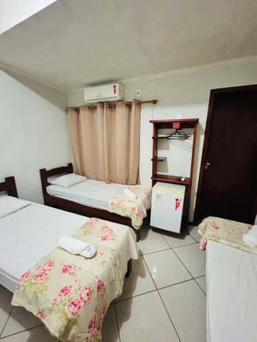 a room with two beds and a refrigerator in it at Hotel Akuto's in Aparecida