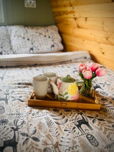 a tray with three cups and flowers on a bed at Knockmany View Glamping in Augher