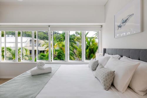 a bedroom with a white bed and large windows at Balboa Apartments in Port Douglas