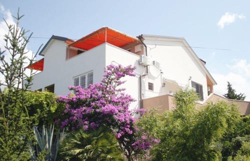 uma casa branca com um telhado vermelho e flores roxas em Apartments Rebac em Murter