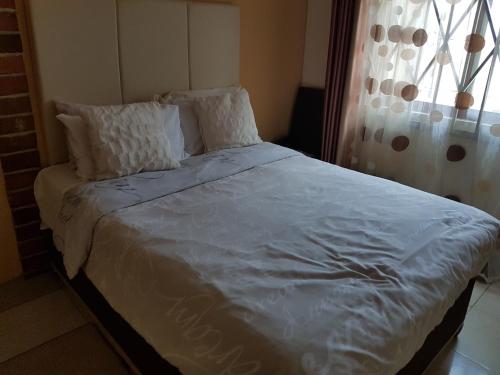 a bed with white sheets and pillows next to a window at Rugems Executive Lodge in Lusaka