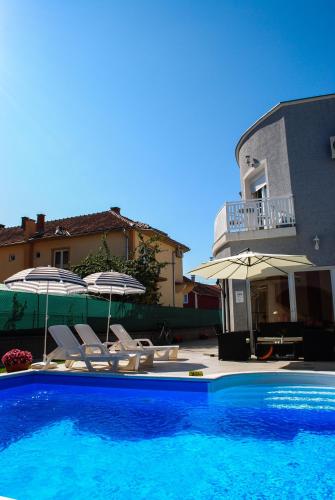 a swimming pool with chairs and umbrellas next to a building at Vila DeLux in Negotin